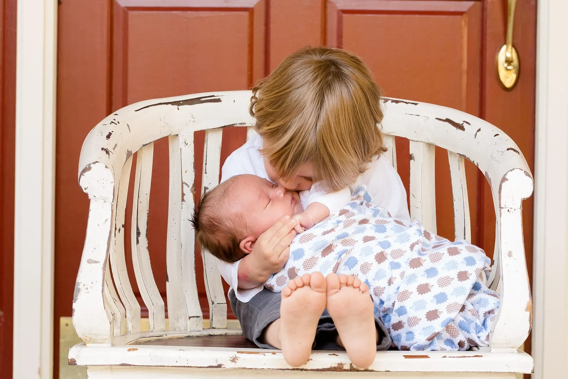 An older child holding and kissing a newborn on a bench