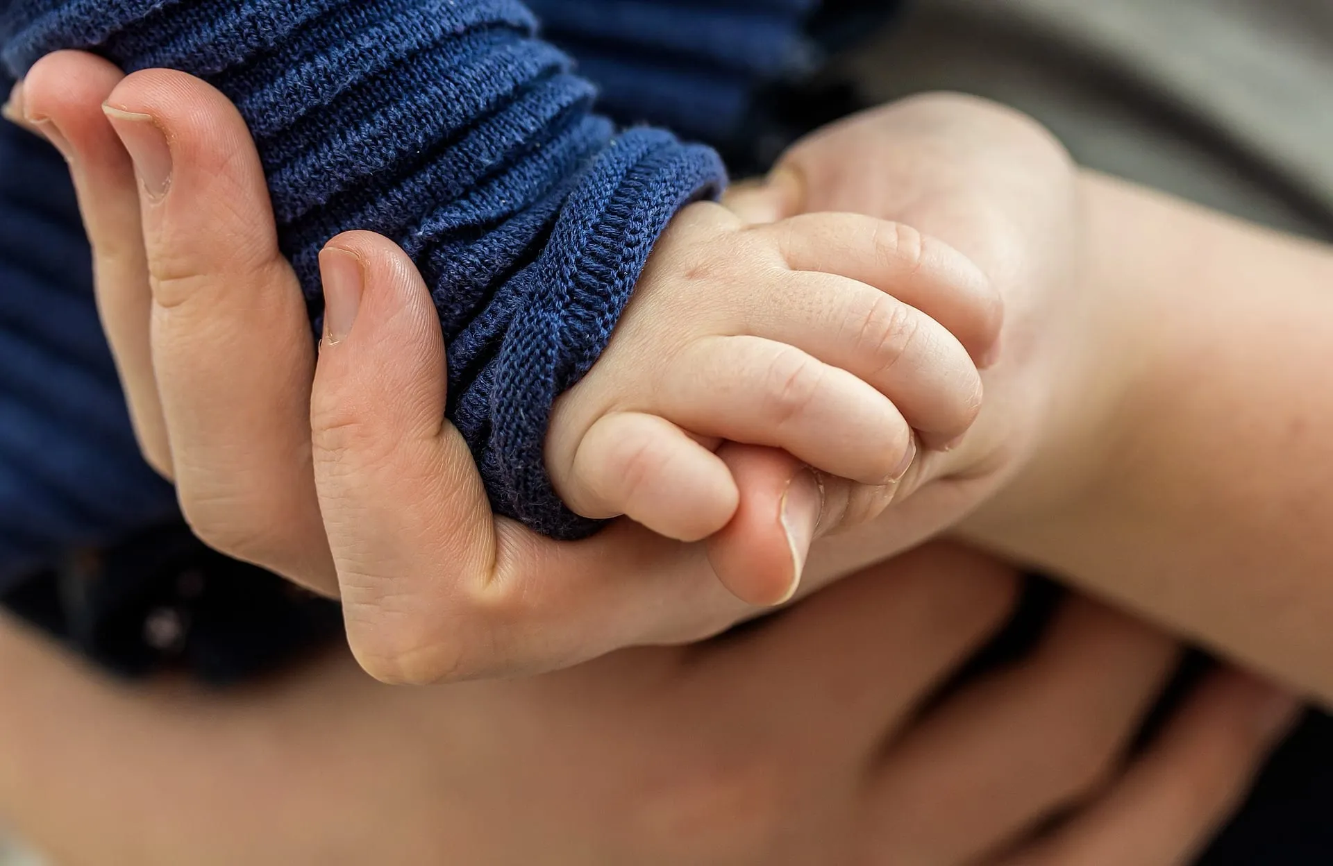 An adult hand holding a newborn baby's hand